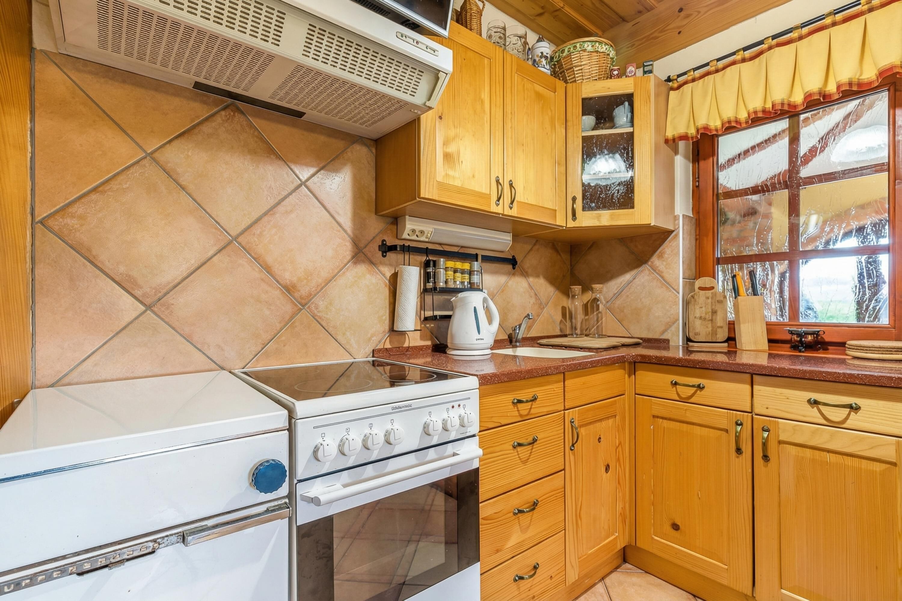 A kitchen with a white stove, wooden cabinets, a window with a curtain, and a tiled backsplash.