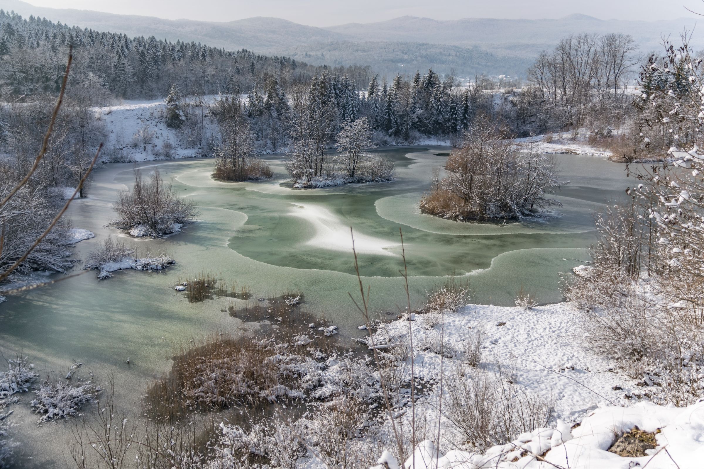 Un paysage hivernal avec une rivi ère gelée, des arbres recouverts de neige et une chaîne de montagnes lointaine.
