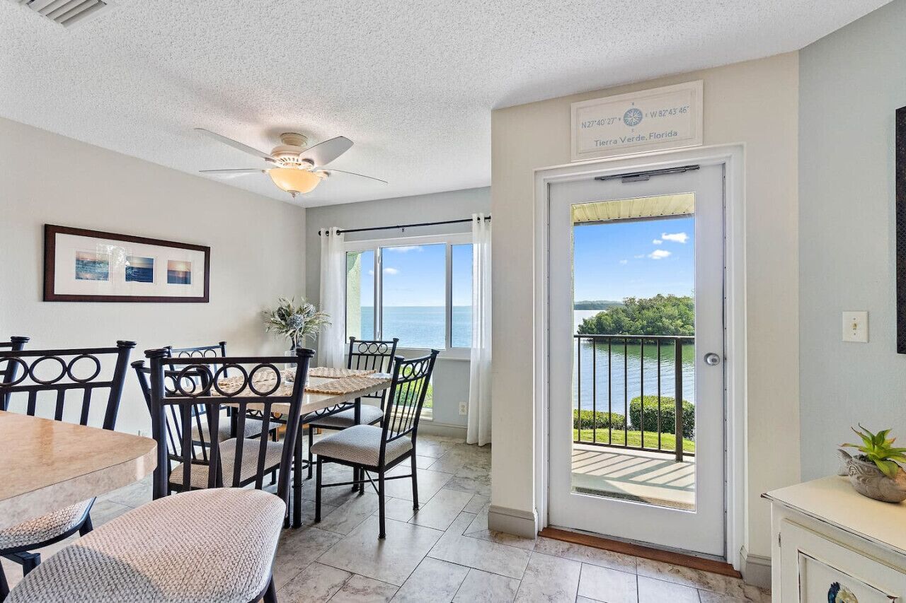 A dining area with a table and chairs, a ceiling fan, and a view of the ocean through a door.