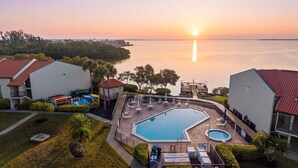 Un resort con una gran piscina, un muelle y vistas al atardecer sobre el agua.