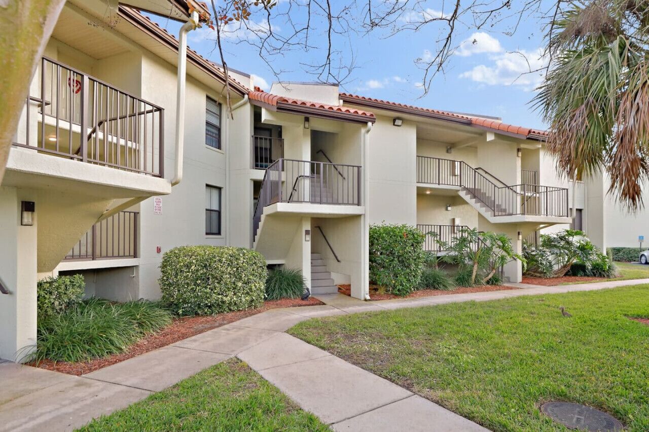 Un edificio residencial de varios pisos con balcones, una escalera central y un césped bien cuidado.