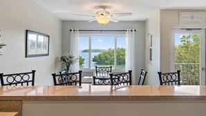 Comedor con vistas a un lago y montañas, ventilador de techo y puerta con un cartel que indica la ubicación.
