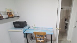 A compact kitchen with a microwave, a small refrigerator, a table with a blue and white tablecloth, and a chair. A door leads to a bathroom. - Private Suite & Bath  10 min JFK  Flexible Terms (Richmond Hill)