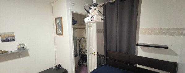 Een slaapkamer met een bed, een nachtkastje, een plank met een discobal, een foto aan de muur en een deur die naar een andere kamer leidt.