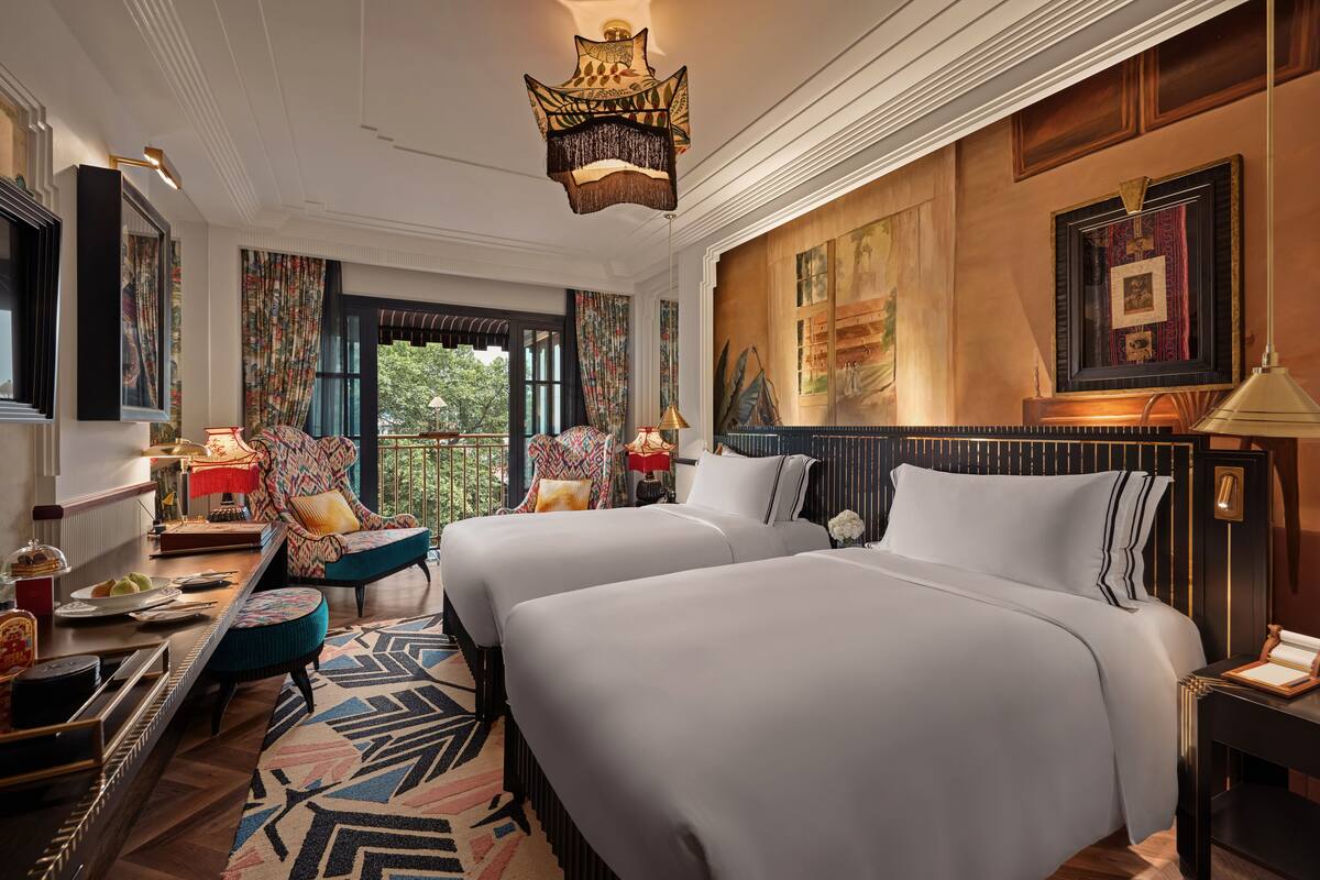 A hotel room with two beds, a desk, a chair, and a large window.