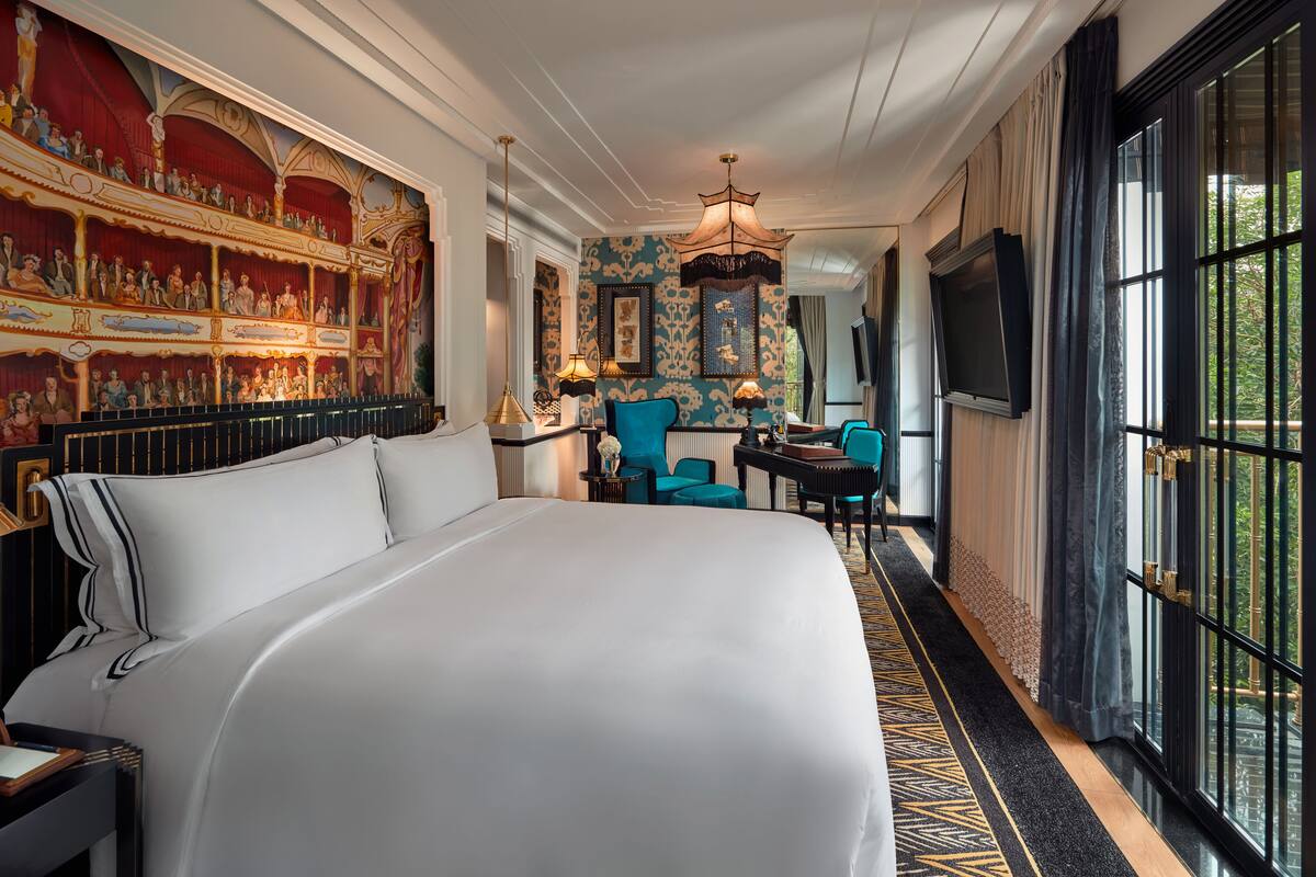 A hotel room with a large bed, a desk with a chair, a television, and a mural on the wall.