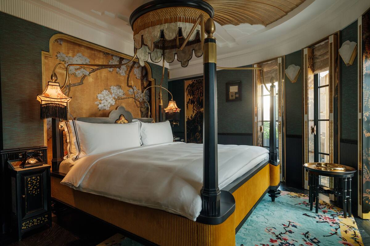 A large bed with a canopy, ornate wall decor, and a classic lamp.
