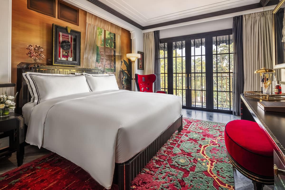 A spacious bedroom with a large bed, a red chair, and a view through a large window.