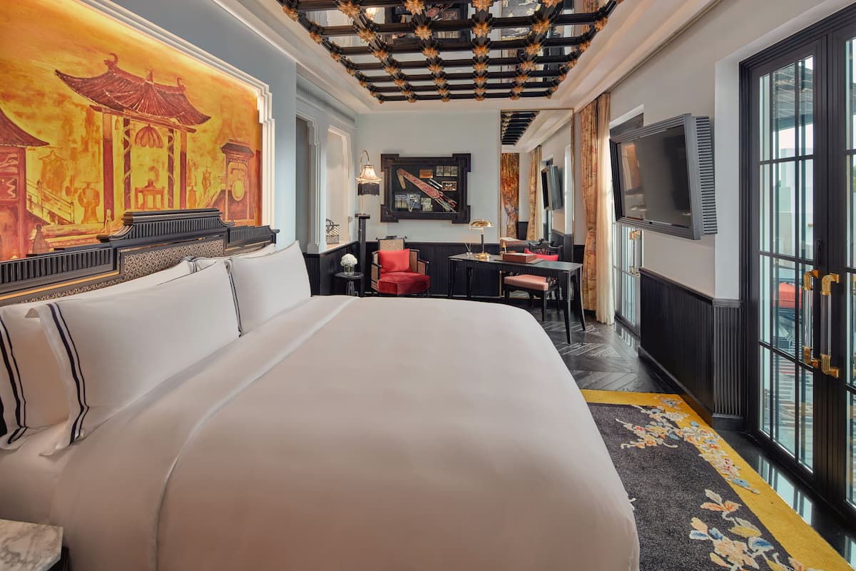 A hotel room with a large bed, a desk, a chair, a TV, and a large window.