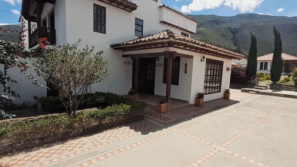 A two-story house with a tiled roof, a covered porch, and a mountain backdrop. - Casa Dalima, home between mountains (Villa de leyva)