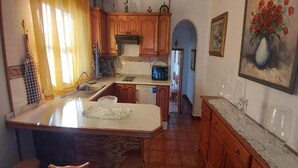 A kitchen with wooden cabinets, a central island, and a dining area with chairs. - Casitas Las Pereras (Los Llanos de Aridane)
