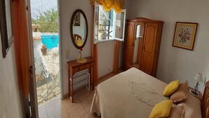 A bedroom with a bed, a desk, a window, a wardrobe, and a door leading to a balcony with a pool. - Casitas Las Pereras (Los Llanos de Aridane)