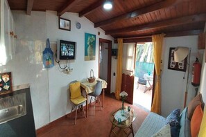 Una habitación acogedora con techo de madera, un área de comedor con mesa y sillas, una cama con almohadones coloridos y un ventanal con cortinas.