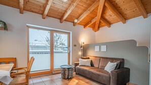 A cozy living room with a wooden ceiling, a sofa, a dining table with chairs, and a view through a glass door. - Detached holiday home in centre of Mittersill (Mittersill)