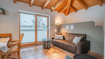 Ein gemütliches Wohnzimmer mit Holzboden, einer Couch, einem Esstisch mit Stühlen und Blick durch eine Glastür.