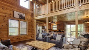 A spacious cabin with a high ceiling, wooden walls, a dining area, and a kitchen. - TWO Cabins!  Sleeps 24, Themed Bunk Rooms for The Kids, Hot Tubs, Mountain Views (Sevierville)