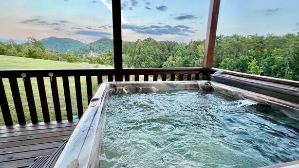 A hot tub with a wooden deck and a view of a forested hillside. - TWO Cabins!  Sleeps 24, Themed Bunk Rooms for The Kids, Hot Tubs, Mountain Views (Sevierville)