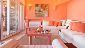 A modern living room with a glass door leading to a stone wall, a white sofa with orange pillows, a glass coffee table, and a painting on the wall. - Luxurious apartment "Piccolo Pevero retreat" with sea view, balcony and terrace (Porto Cervo)