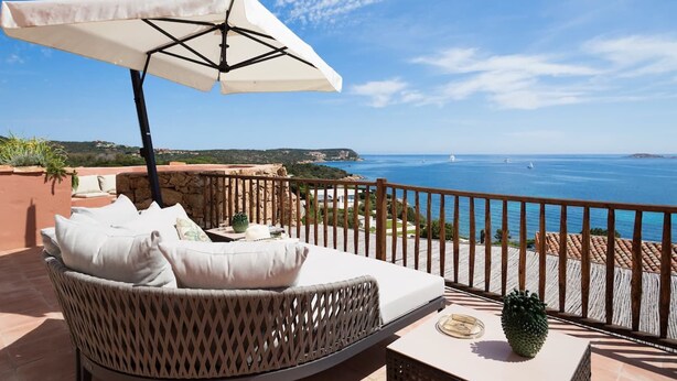 A balcony with a wicker sofa, a table, and a large umbrella. - Luxurious apartment "Piccolo Pevero retreat" with sea view, balcony and terrace (Porto Cervo)