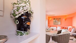 A room with a white wall, a decorative ceramic head sculpture, a dining table, and a sofa with orange cushions. - Luxurious apartment "Piccolo Pevero retreat" with sea view, balcony and terrace (Porto Cervo)