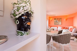Una habitación con pared blanca, una escultura de cabeza de cerámica decorativa, una mesa de comedor y un sofá con cojines naranjas.