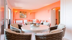A modern interior with a round dining table, cushioned chairs, a sofa with orange cushions, and a painting on the wall. - Luxurious apartment "Piccolo Pevero retreat" with sea view, balcony and terrace (Porto Cervo)