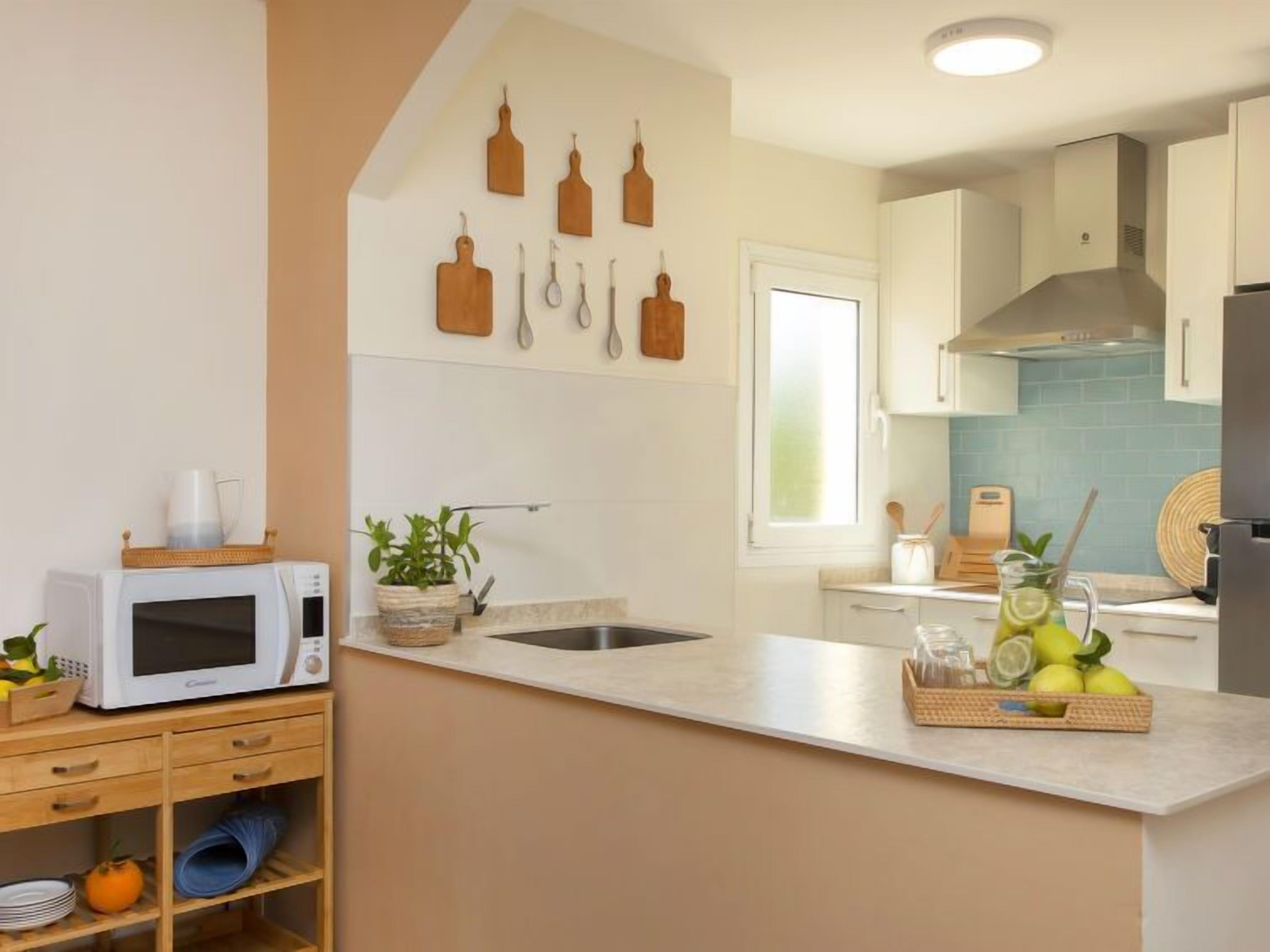Una cocina con microondas, pileta y ventana. Hay utensilios de madera colgados en la pared y una cesta de limones en la encimera.