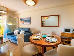 A dining area with a round table set for four, a sofa, a television, and a window with curtains.