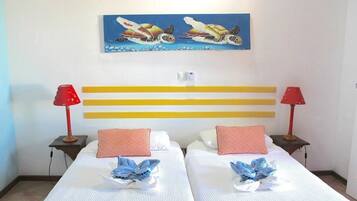 Habitación de hotel con dos camas, cada una con una lámpara roja, un cuadro de tortugas marinas en la pared y un cabecero sencillo.