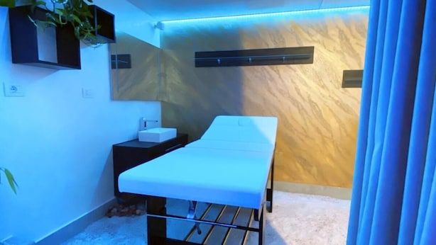 Un consultorio médico con una cama, un escritorio, una planta y una pared de madera.