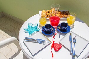 Mesa redonda servida con alimentos para el desayuno, incluyendo pasteles, una decoración con forma de estrella de mar y un objeto con forma de corazón, además de cubiertos y vasos.