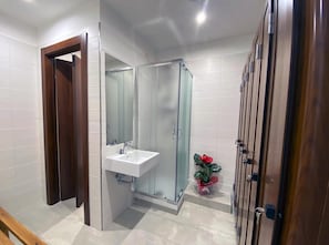 Un baño moderno con cabina de ducha de vidrio, un lavabo blanco y una puerta de madera.