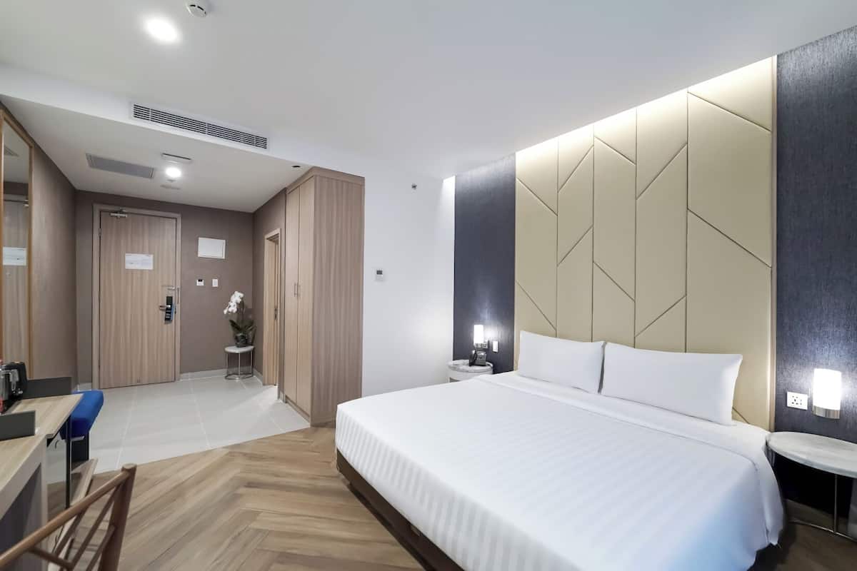 A modern hotel room with a large bed, a desk, and a wardrobe.