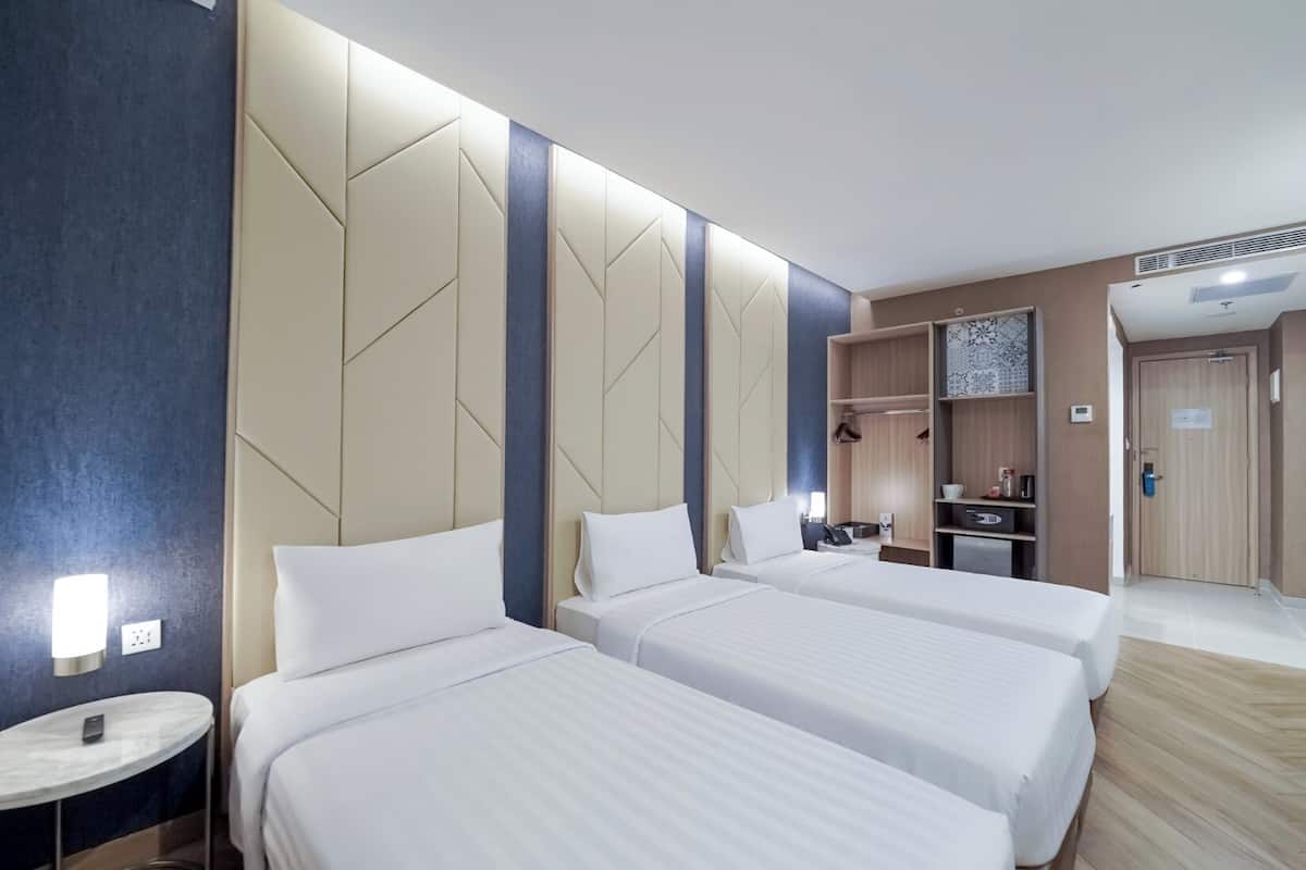 A hotel room with three beds, a small round table, a wardrobe, and a kitchenette.