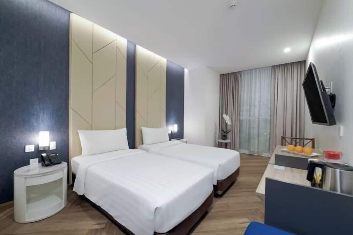 A hotel room with two beds, a desk with a chair, a TV, and a small table with fruit.