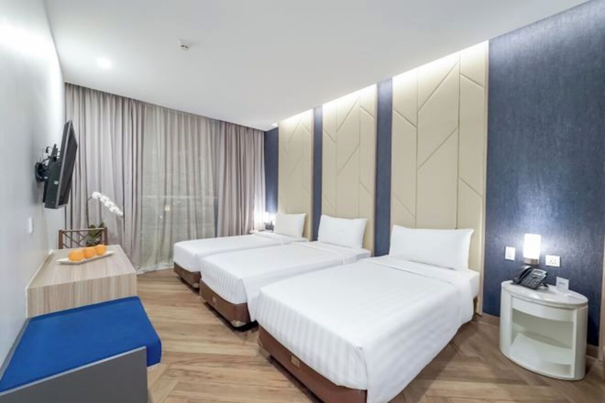 A hotel room with two beds, a desk, a chair, a TV, and a bedside table with a lamp.