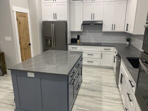 A modern kitchen with white cabinets, a marble countertop, and a stainless steel refrigerator. - Lake View Modern House with Beautiful Sunsets! (Page)
