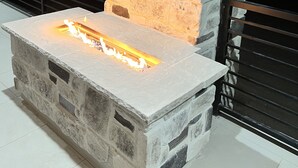 A stone fireplace with a fire burning inside, set against a dark background. - Lake View Modern House with Beautiful Sunsets! (Page)