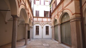 A courtyard with stone columns, arched doorways, and a cobblestone floor. - San Maurilio  Apartment (Milano)
