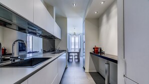 A modern kitchen with a long countertop, a built-in oven, and a dining area with a table and chairs. - San Maurilio  Apartment (Milano)