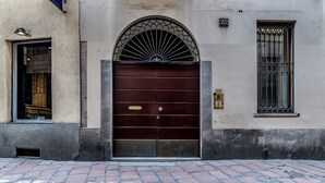 A building with a large, dark wooden door, a small window with a metal grill, and a brick-paved ground. - San Maurilio  Apartment (Milano)