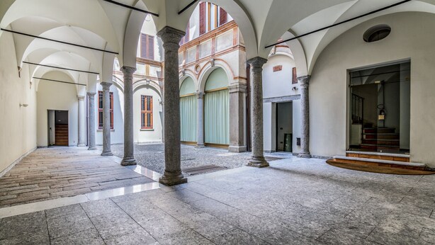 A spacious interior with high ceilings, stone columns, and a central open area with a tiled floor. - San Maurilio  Apartment (Milano)