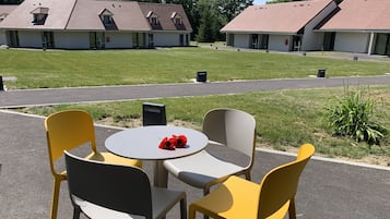Un patio con una mesa redonda y cuatro sillas, un pequeño jardín y un edificio con techo rojo al fondo.