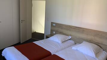 Hotelkamer met twee bedden, een houten hoofdbord, een deur en uitzicht op een gang.