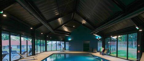 Una piscina interior con paredes de vidrio transparente, techo azul y vistas al exterior.