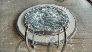 Ein Whirlpool mit strukturierter Kante und Metallhandläufen, umgeben von einer Ziegelterrasse.