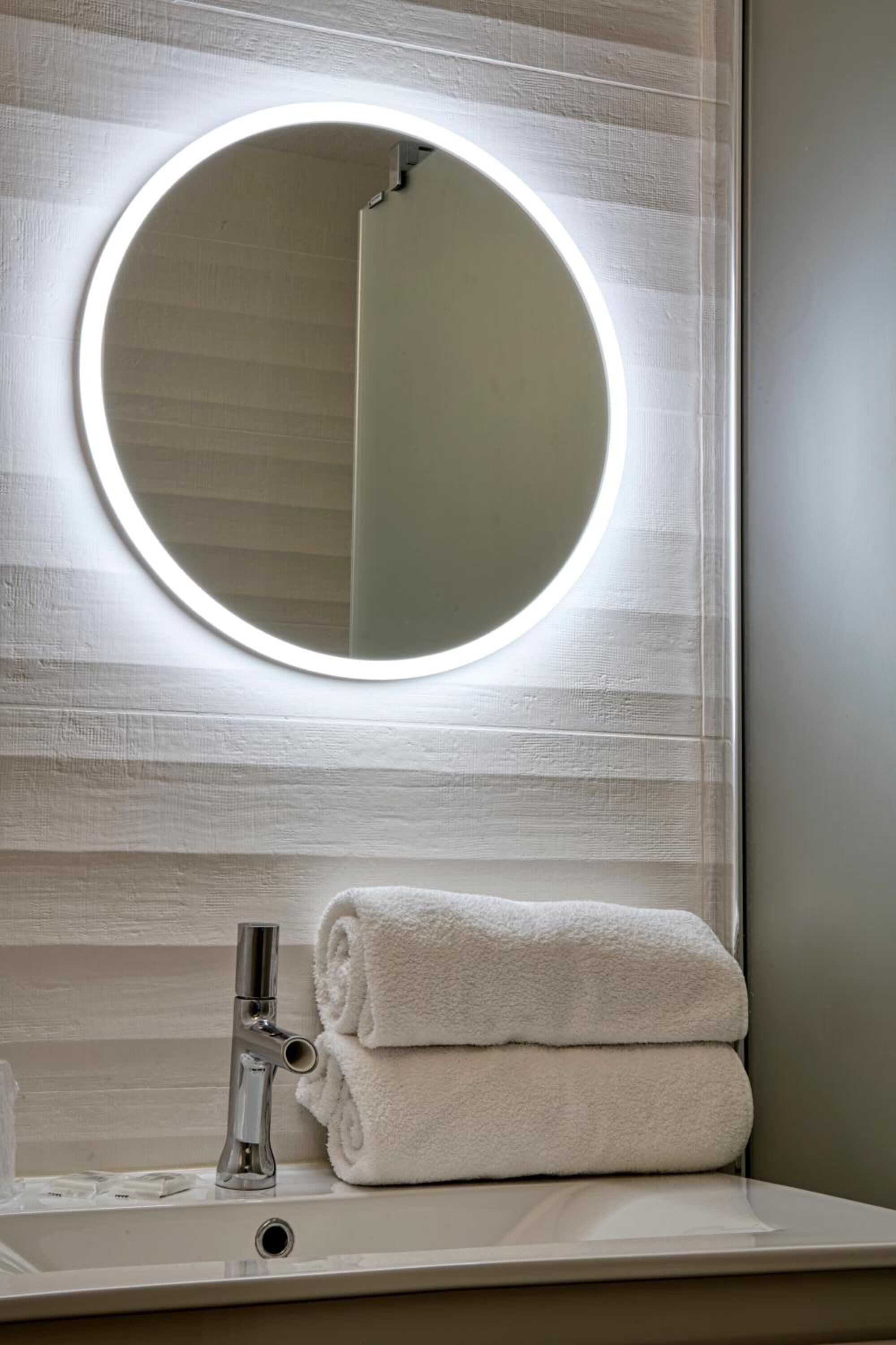 A bathroom with a round mirror, a sink, and a towel.