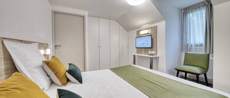 A hotel room with a bed, a desk, a chair, and a television.