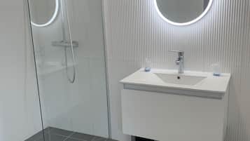 A modern bathroom with a glass-enclosed shower, a white sink with a round mirror, and a tiled floor.