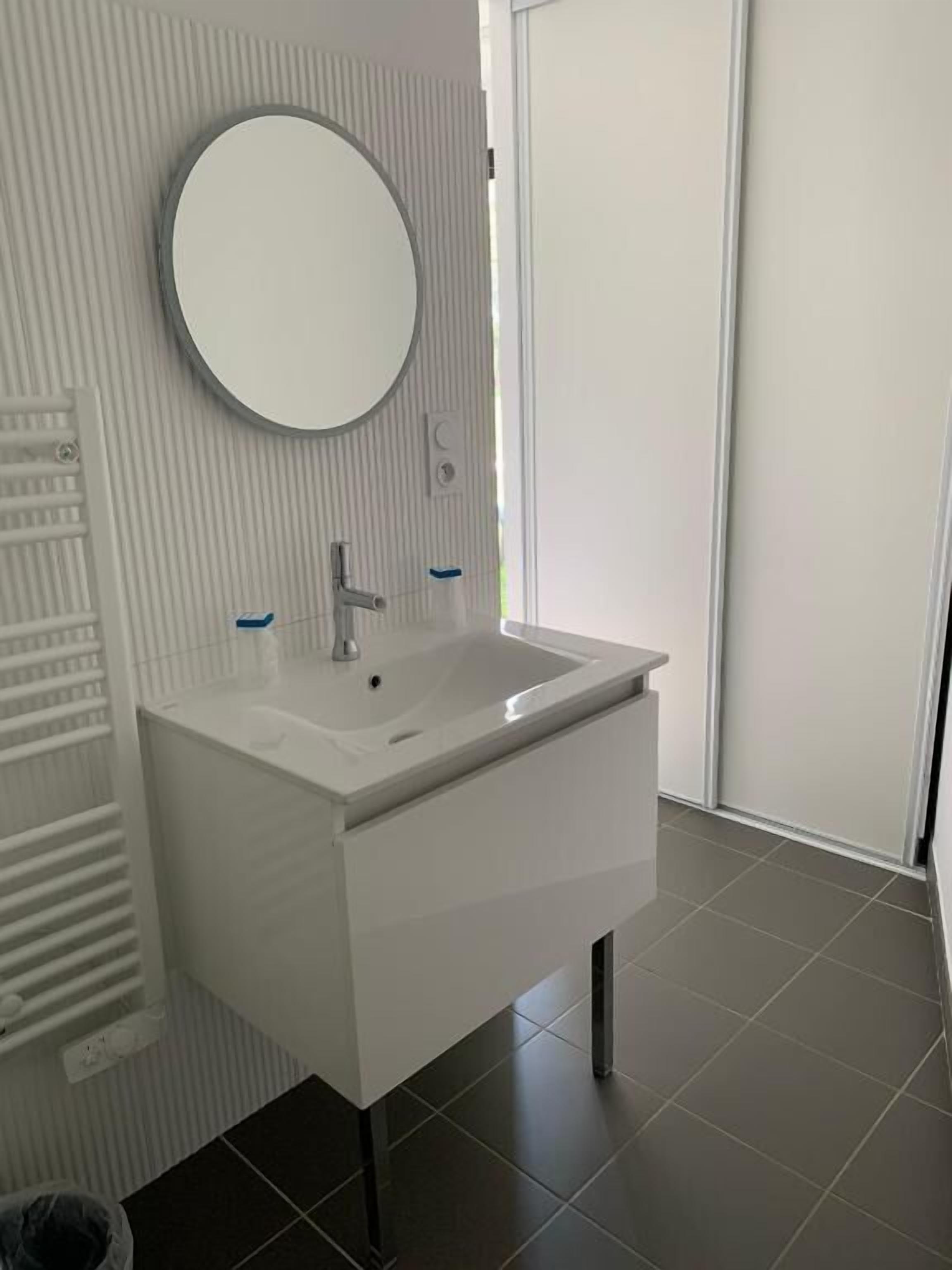Une salle de bain moderne avec un meuble-lavabo blanc, un miroir rond et un radiateur encastré.